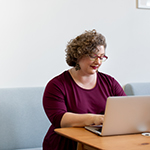 "woman smiling and writing on a laptop"