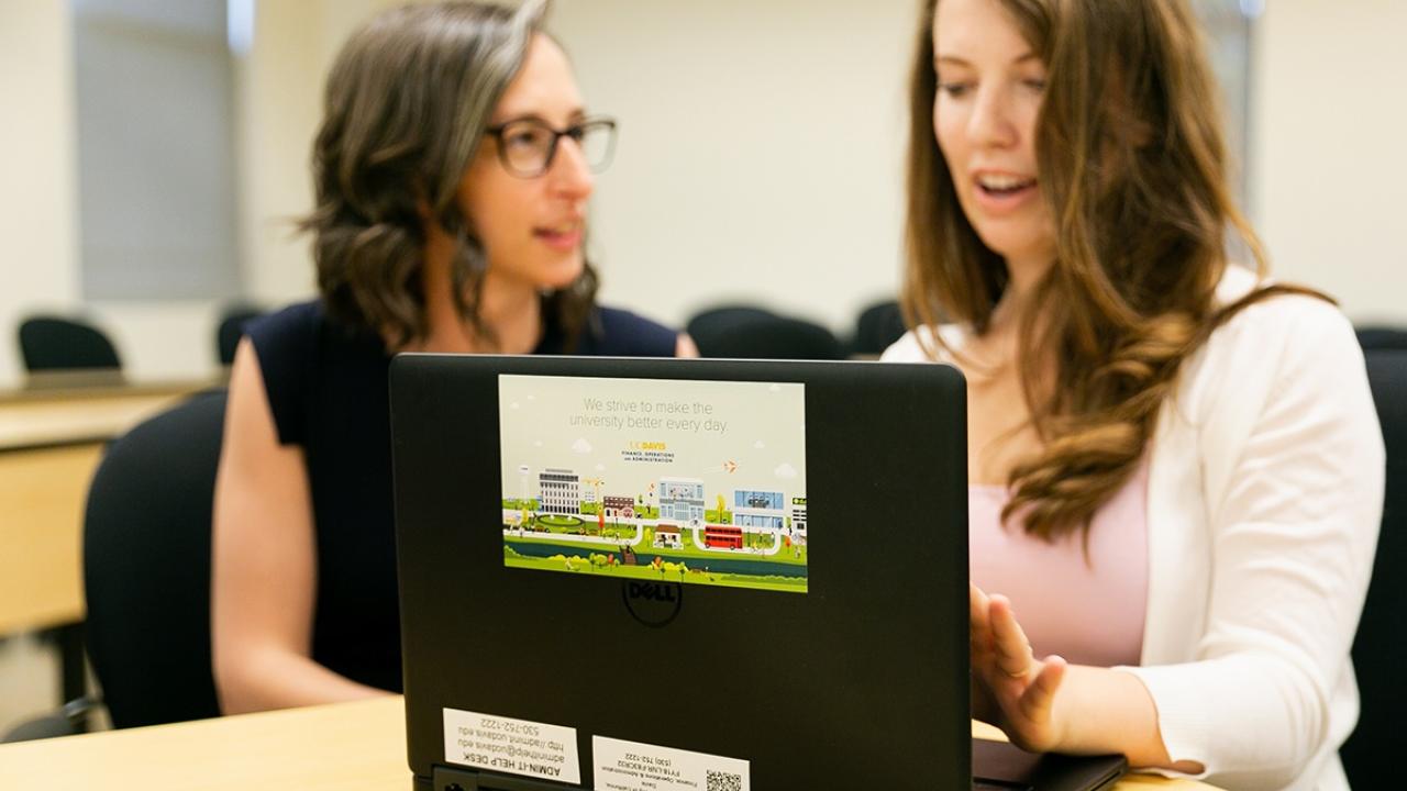 two people looking at a laptop. One person is typing,