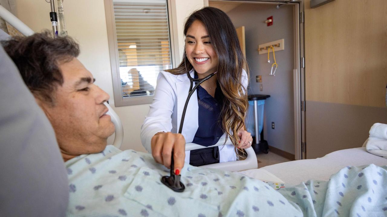 Female doctor has her stethoscope out checking a man's heartbeat. The man is a patient laying in bed.