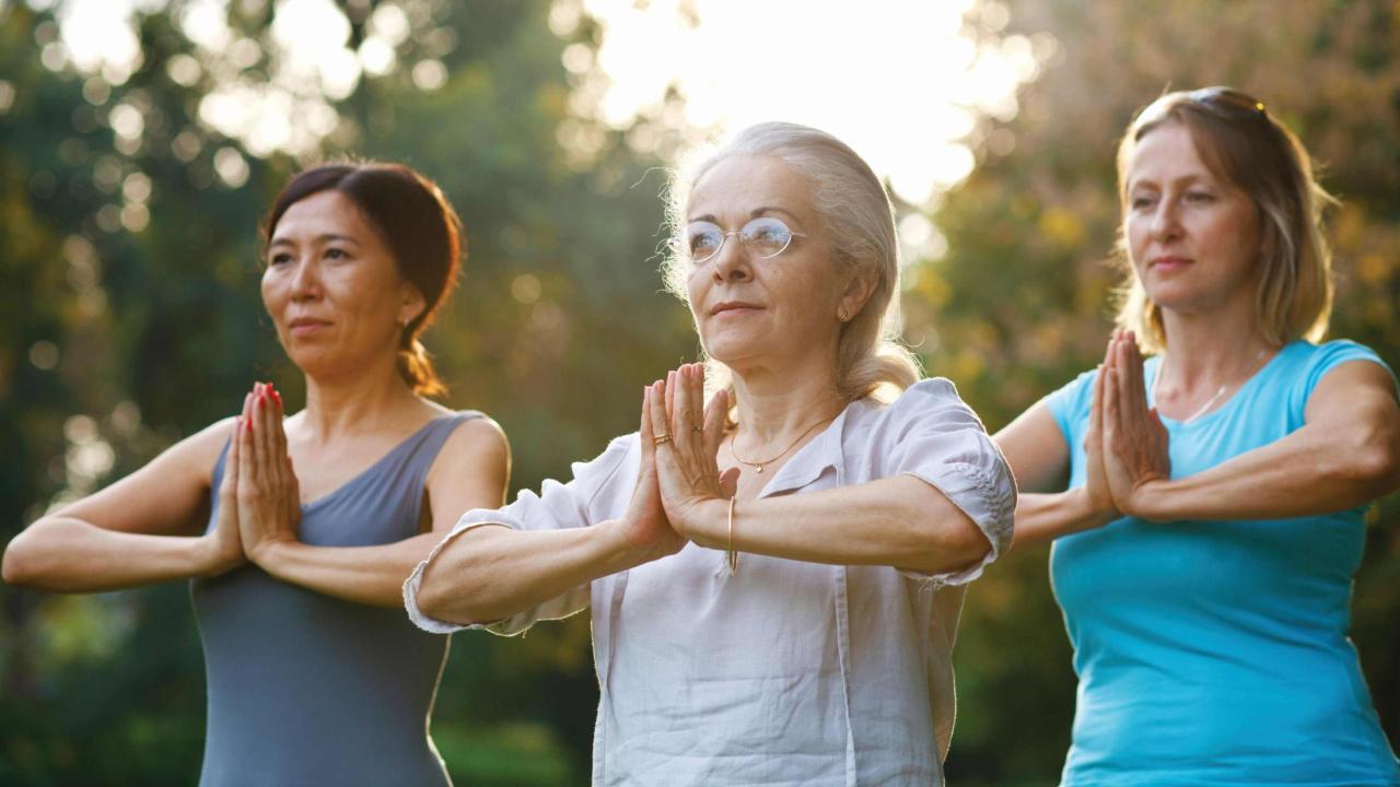 Three women are doing a yoga pose outdoors.  