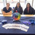 Rachel Henry, Melissa Cuevas, and Jasmine Cusic from the Workplace Violence Prevention team are seated at a table with materials in front of them.  